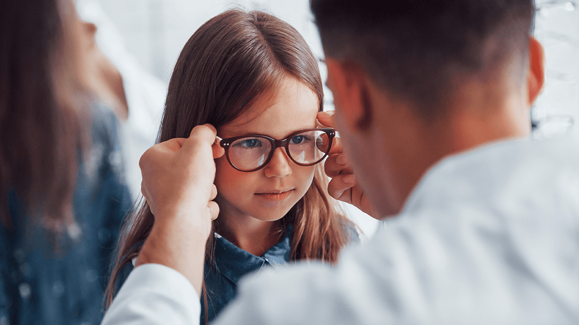 Young pediatrician in white coat helps to get new glasses for little girl.